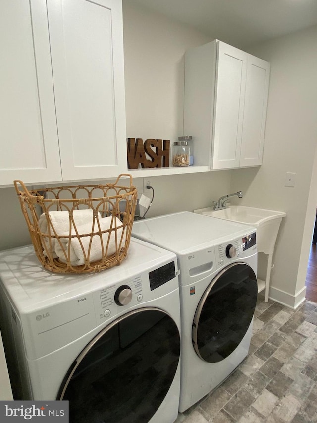 washroom featuring independent washer and dryer, a sink, cabinet space, and baseboards