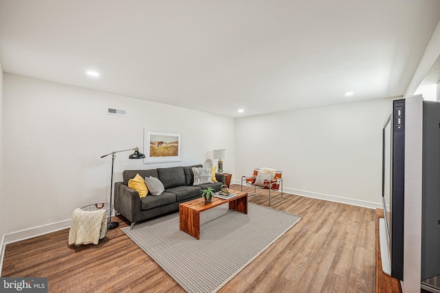 living room featuring baseboards, visible vents, wood finished floors, and recessed lighting