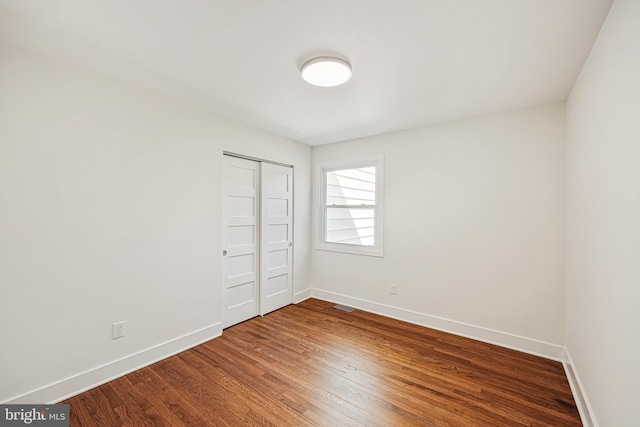 unfurnished bedroom with a closet, wood finished floors, visible vents, and baseboards