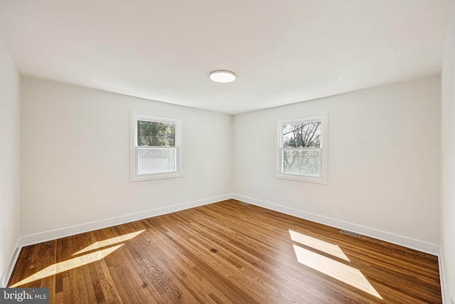 spare room with visible vents, wood finished floors, a wealth of natural light, and baseboards