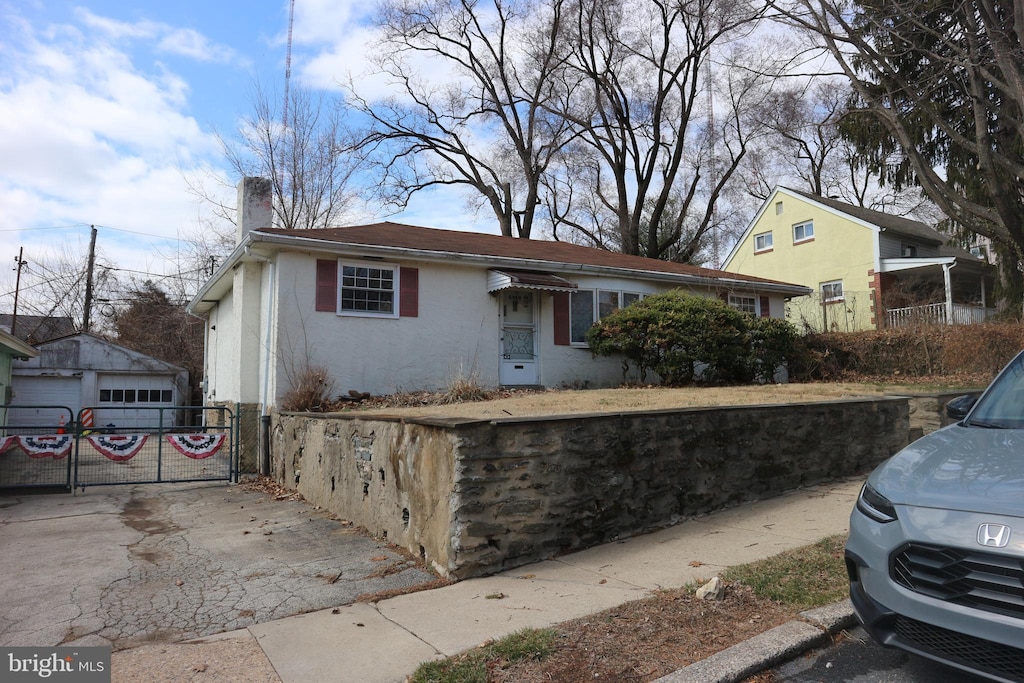 view of front of home featuring driveway, a chimney, a detached garage, a gate, and stucco siding