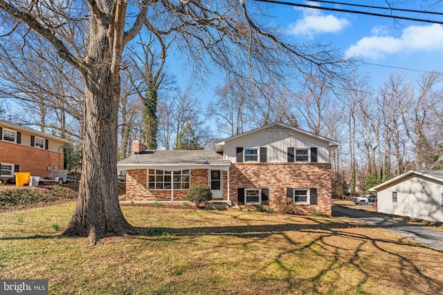 split level home featuring a front lawn, brick siding, and a chimney