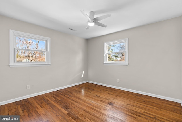 empty room with ceiling fan, visible vents, baseboards, and wood finished floors