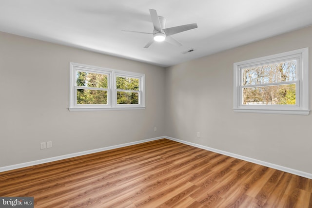 empty room with light wood-style floors, a healthy amount of sunlight, visible vents, and baseboards