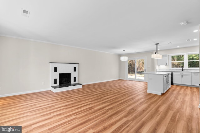 unfurnished living room with visible vents, light wood-style flooring, a sink, baseboards, and a brick fireplace