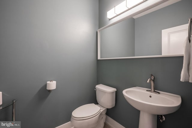 half bath with a sink, baseboards, and toilet