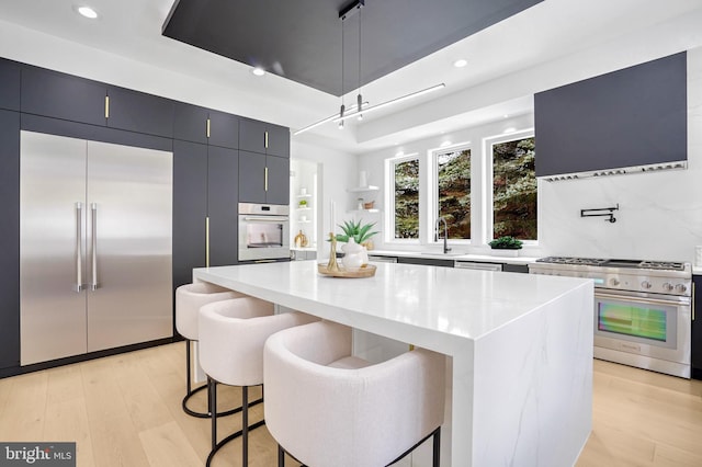 kitchen featuring premium appliances, a kitchen island, light wood-type flooring, dark cabinetry, and a kitchen bar