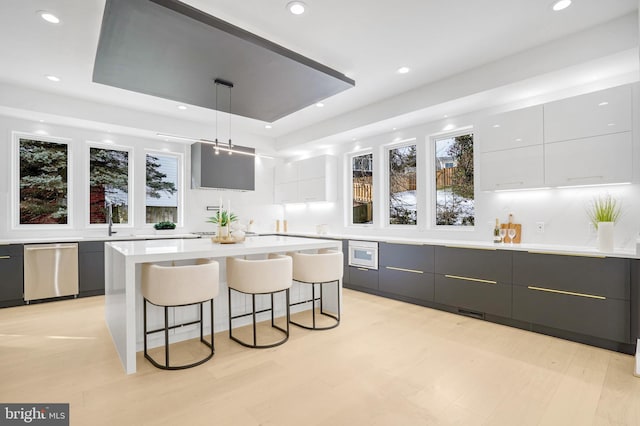 bar with a raised ceiling, dishwasher, light wood-style flooring, pendant lighting, and recessed lighting