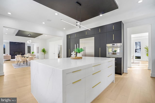 kitchen with built in fridge, white oven, light wood finished floors, modern cabinets, and dark cabinetry