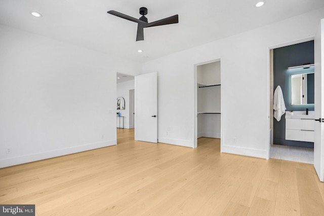 unfurnished bedroom with a walk in closet, light wood finished floors, recessed lighting, ensuite bathroom, and baseboards