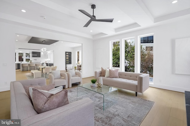 living area featuring recessed lighting, a raised ceiling, light wood-style floors, a ceiling fan, and baseboards