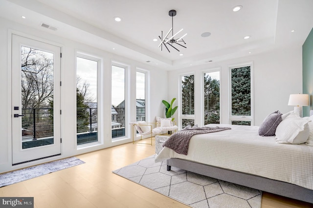 bedroom with access to outside, a tray ceiling, wood finished floors, and recessed lighting