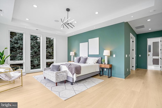 bedroom featuring a notable chandelier, light wood-style flooring, visible vents, and a tray ceiling