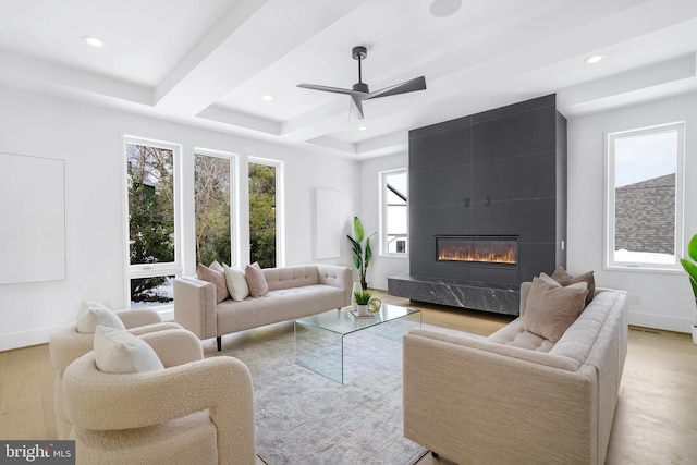 living room with a premium fireplace, a tray ceiling, wood finished floors, and recessed lighting