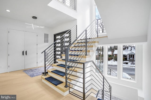 stairway featuring recessed lighting, a high ceiling, a wealth of natural light, and wood finished floors