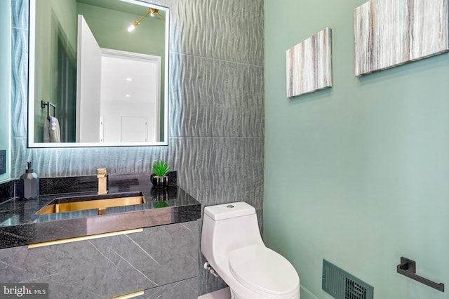 bathroom with toilet, vanity, visible vents, and tile walls