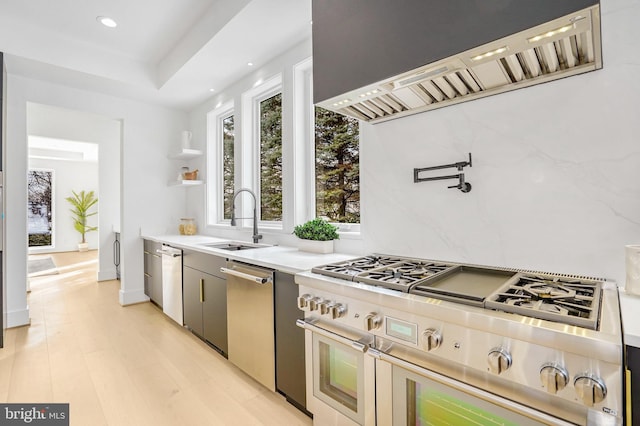 kitchen with extractor fan, stainless steel appliances, a sink, light wood-style floors, and light countertops