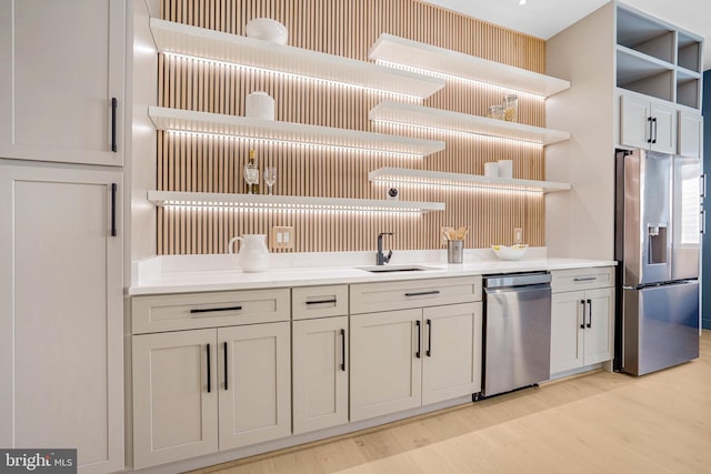 kitchen with a sink, light wood-style floors, light countertops, appliances with stainless steel finishes, and open shelves