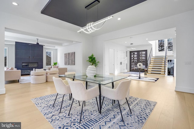 dining area featuring a premium fireplace, stairway, wood finished floors, and recessed lighting