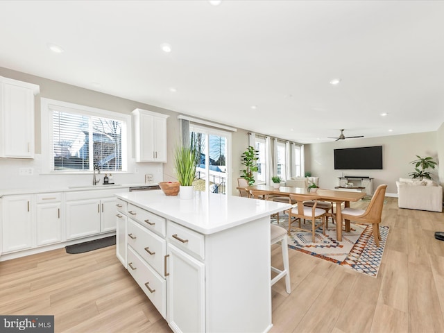 kitchen with recessed lighting, a sink, a kitchen island, white cabinetry, and light wood-type flooring