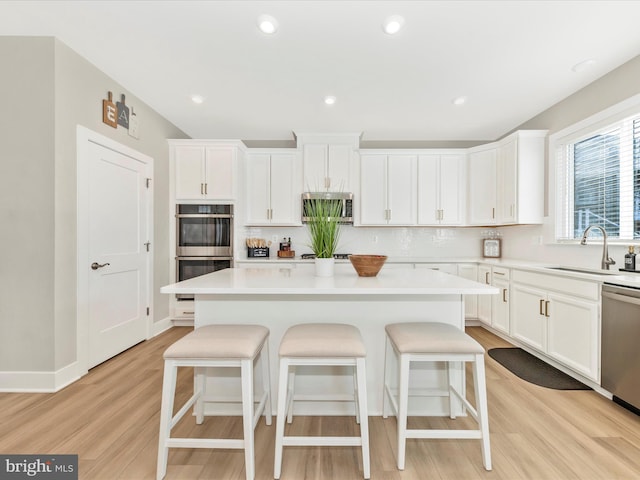 kitchen featuring light wood-style flooring, a sink, white cabinetry, appliances with stainless steel finishes, and a kitchen bar