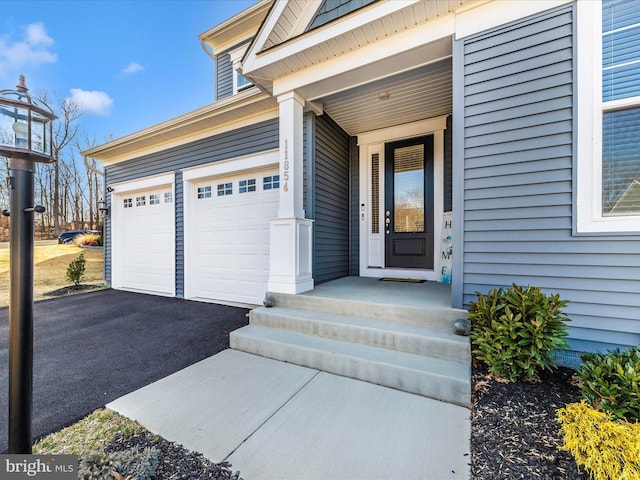 view of exterior entry featuring a garage and aphalt driveway