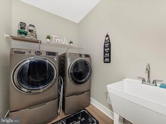 clothes washing area featuring washing machine and dryer, laundry area, a sink, baseboards, and light wood finished floors