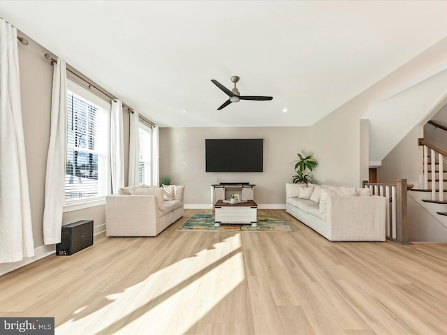 living room with a ceiling fan, stairway, baseboards, and wood finished floors