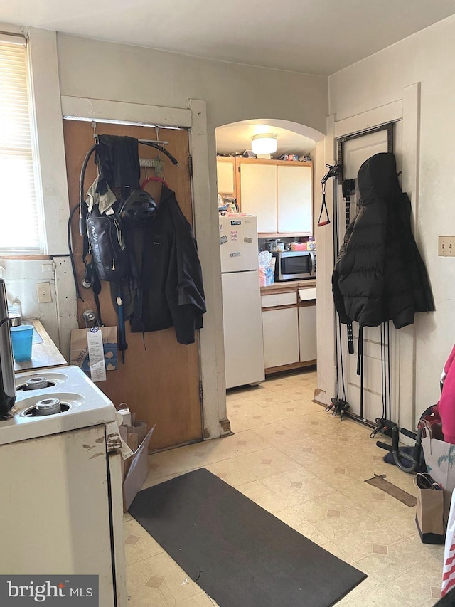 kitchen featuring stainless steel microwave, arched walkways, light floors, and freestanding refrigerator