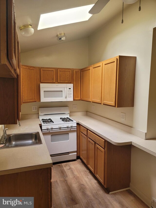 kitchen with lofted ceiling with skylight, white appliances, a sink, and wood finished floors