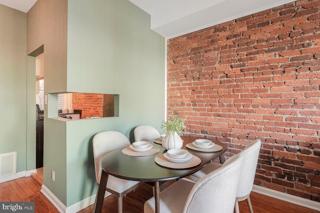 dining area featuring visible vents, baseboards, wood finished floors, and brick wall