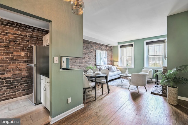 living area featuring light wood finished floors, brick wall, an accent wall, and baseboards