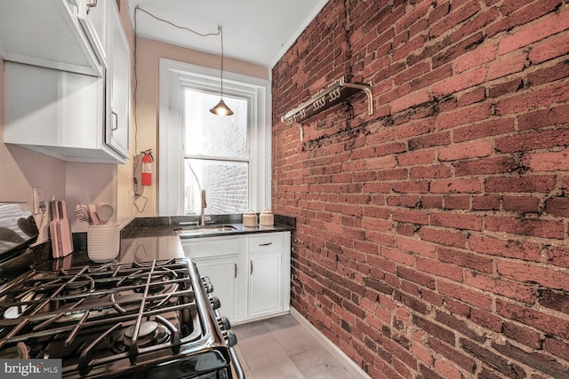 kitchen with brick wall, a sink, black gas range, white cabinetry, and dark countertops