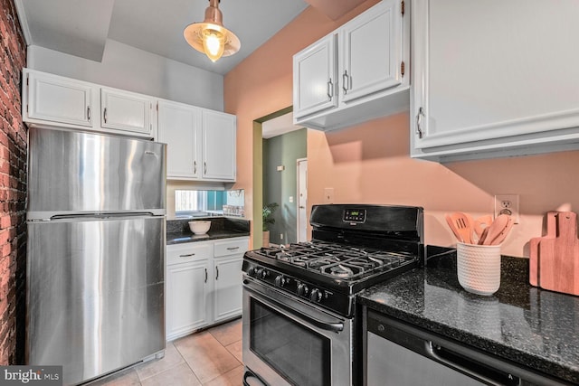 kitchen featuring brick wall, light tile patterned floors, dark stone countertops, appliances with stainless steel finishes, and white cabinets