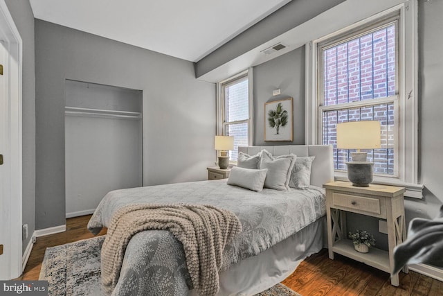 bedroom with a closet, visible vents, baseboards, and wood finished floors