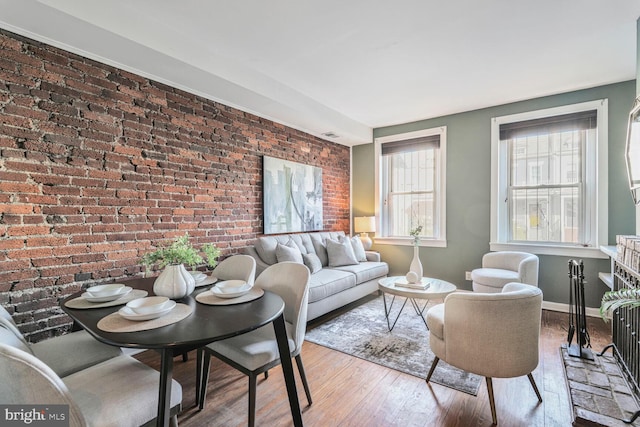 living area featuring baseboards, wood finished floors, and brick wall