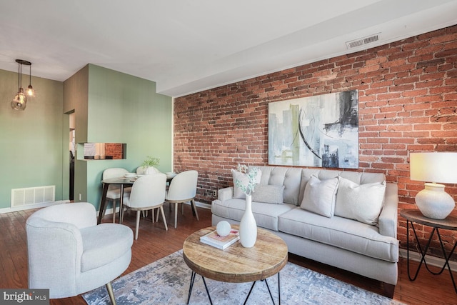 living room with visible vents, baseboards, wood finished floors, and brick wall