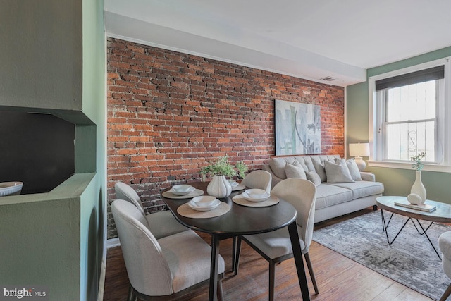 dining room featuring visible vents, wood finished floors, and brick wall