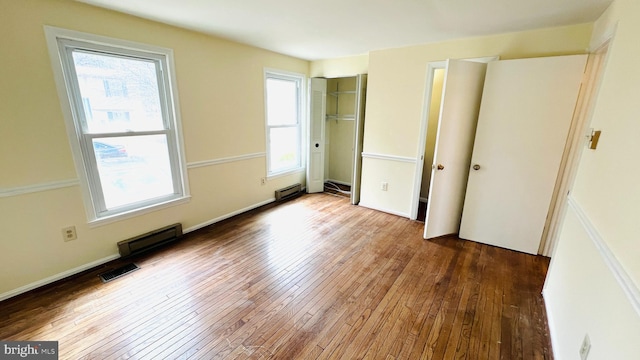 unfurnished bedroom featuring a baseboard heating unit, wood-type flooring, visible vents, and a closet