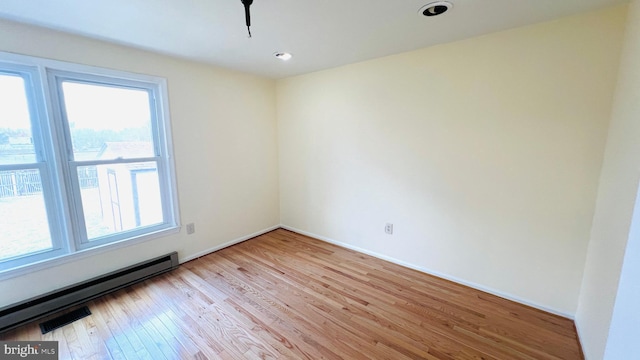 empty room featuring baseboard heating, light wood-type flooring, visible vents, and baseboards