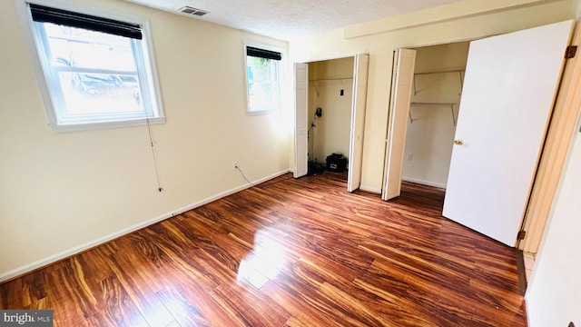 unfurnished bedroom with multiple closets, visible vents, a textured ceiling, wood finished floors, and baseboards