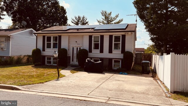 split foyer home featuring fence, a front lawn, and solar panels