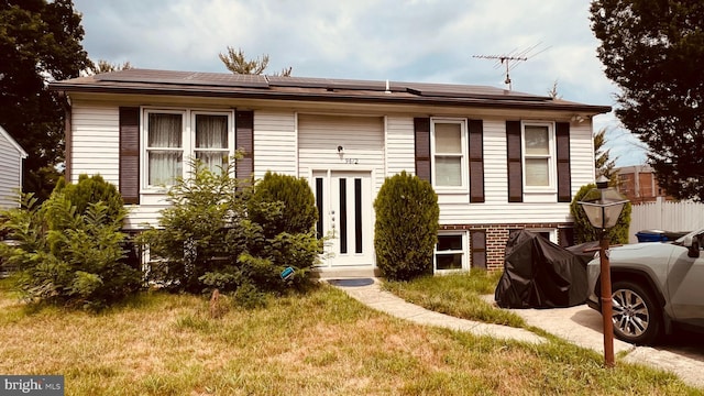 bi-level home with a front lawn and solar panels