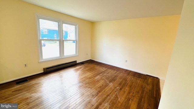 empty room with a baseboard heating unit, visible vents, baseboards, and dark wood-style floors