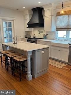 kitchen featuring light wood finished floors, black range with gas stovetop, a center island, light countertops, and custom exhaust hood