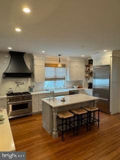 kitchen with custom exhaust hood, high quality appliances, wood finished floors, and light countertops