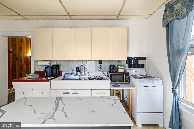 kitchen featuring white range with electric cooktop, stainless steel microwave, cream cabinets, and decorative backsplash