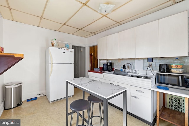 kitchen with freestanding refrigerator, decorative backsplash, light countertops, a paneled ceiling, and stainless steel microwave