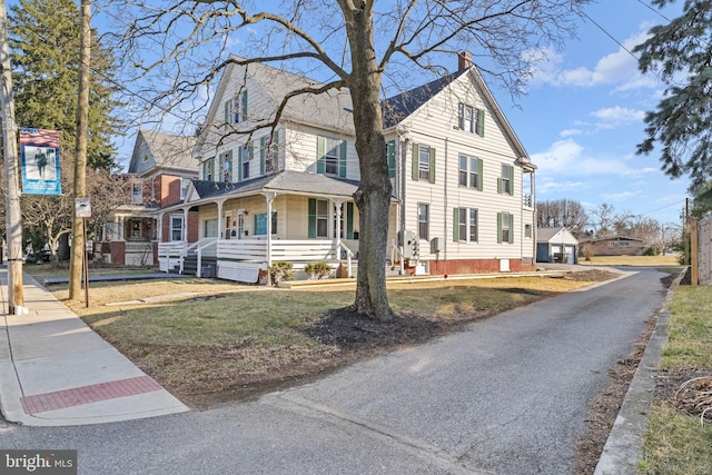 view of front of house with covered porch, a chimney, and a front yard