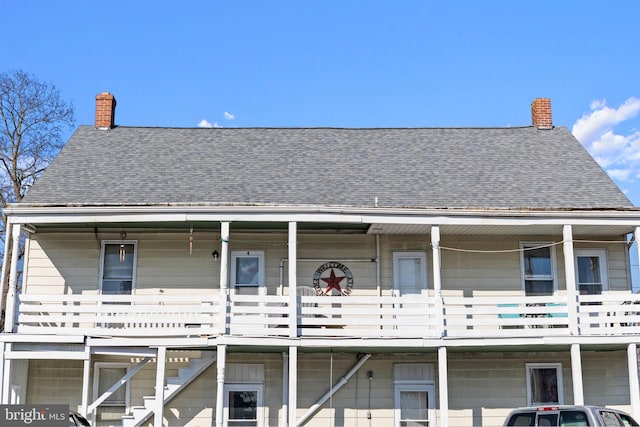 back of property featuring a shingled roof, a porch, and a chimney